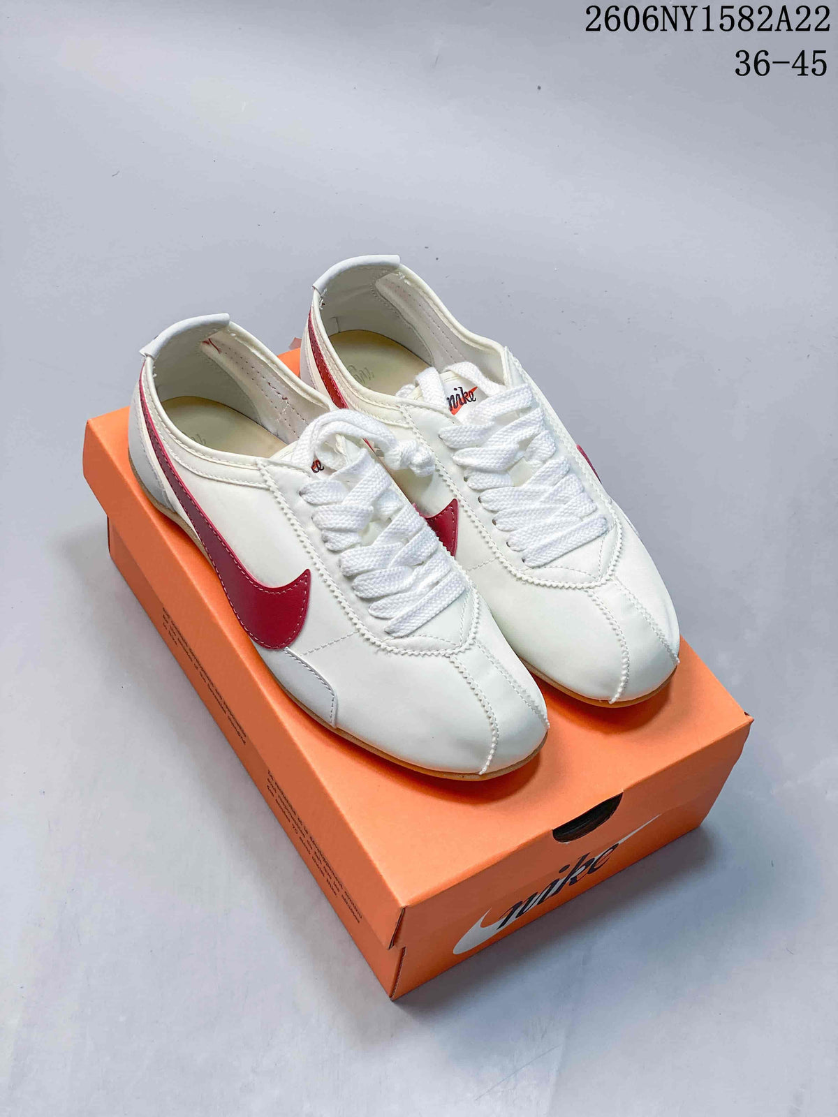 Pair of off-white Nike Moon Shoe OG Summit low-top sneakers with red side details and a gum-colored outsole, shown on an orange box.