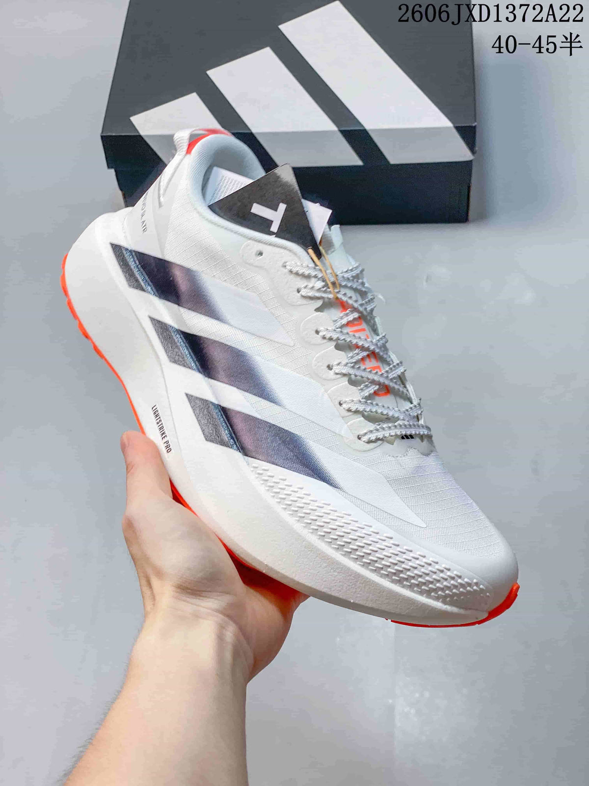 Angled side view of a white Adidas running shoe with dark stripes, textured upper details and orange outsole accents.