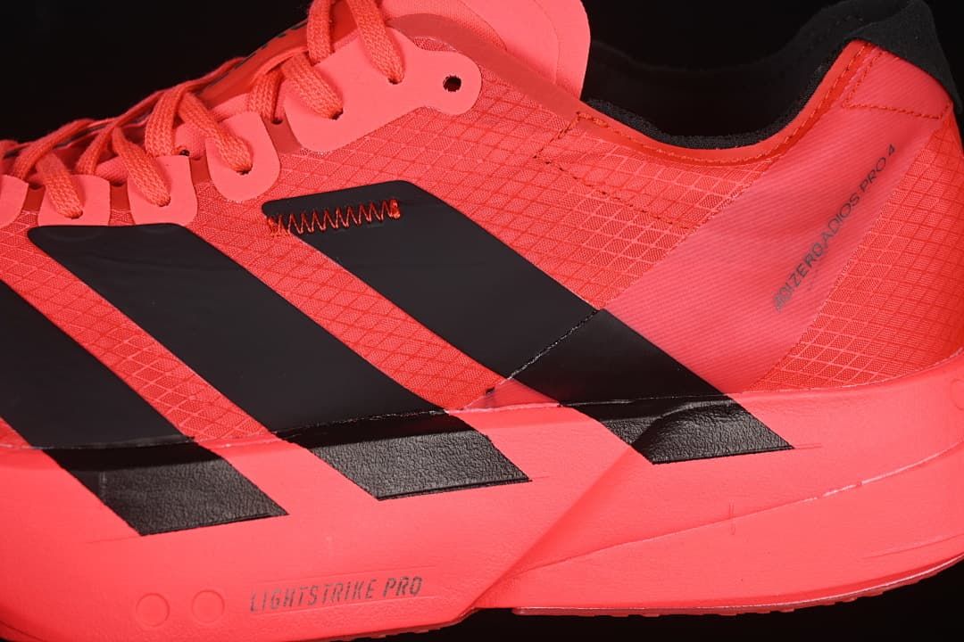 Close-up of coral upper, black stripes, and Adios Pro branding
