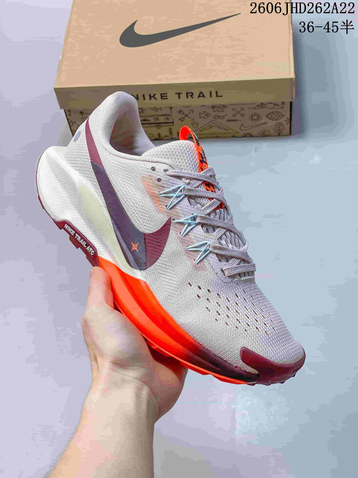 Angled side view of the pale pink and white Nike Pegasus Trail shoe with orange and burgundy accents