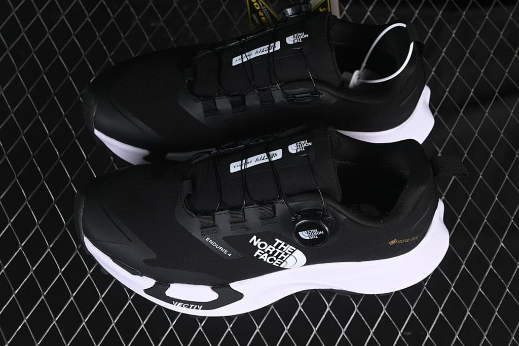 Pair of black low-cut shoes with white midsoles, shown from above.