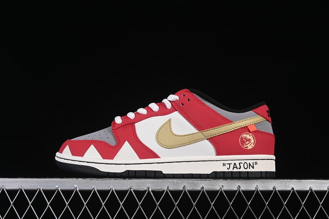 Side view of a red, white, gray, and gold Nike SB Dunk Low with dinosaur-themed details and “JASON” text on the midsole.