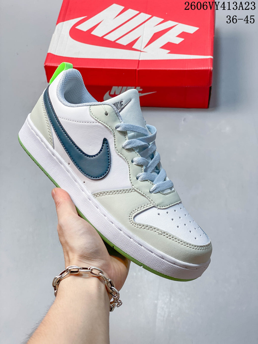 White sneaker with a blue Swoosh, pale green-gray overlays, and bright green outsole accents