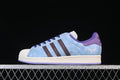 Side profile of a light blue adidas Superstar II sneaker with dark stripes, purple accents and an off-white shell toe