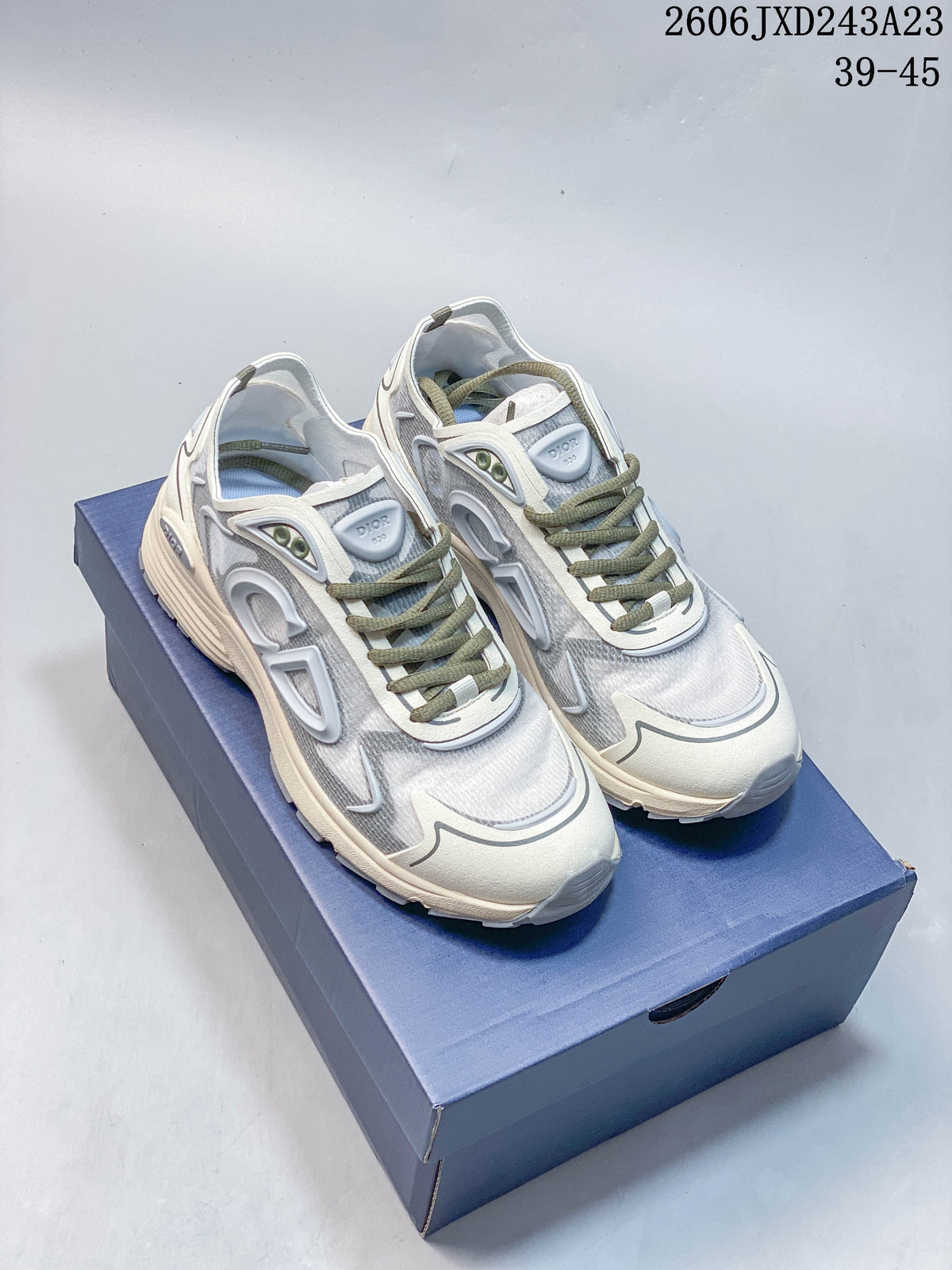 Pair of gray and light-colored Dior B30 low-top sneakers with olive-toned laces, shown on a blue box