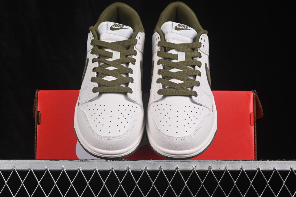 Front view of a pair of white and olive Nike low-top sneakers resting on a red shoebox.