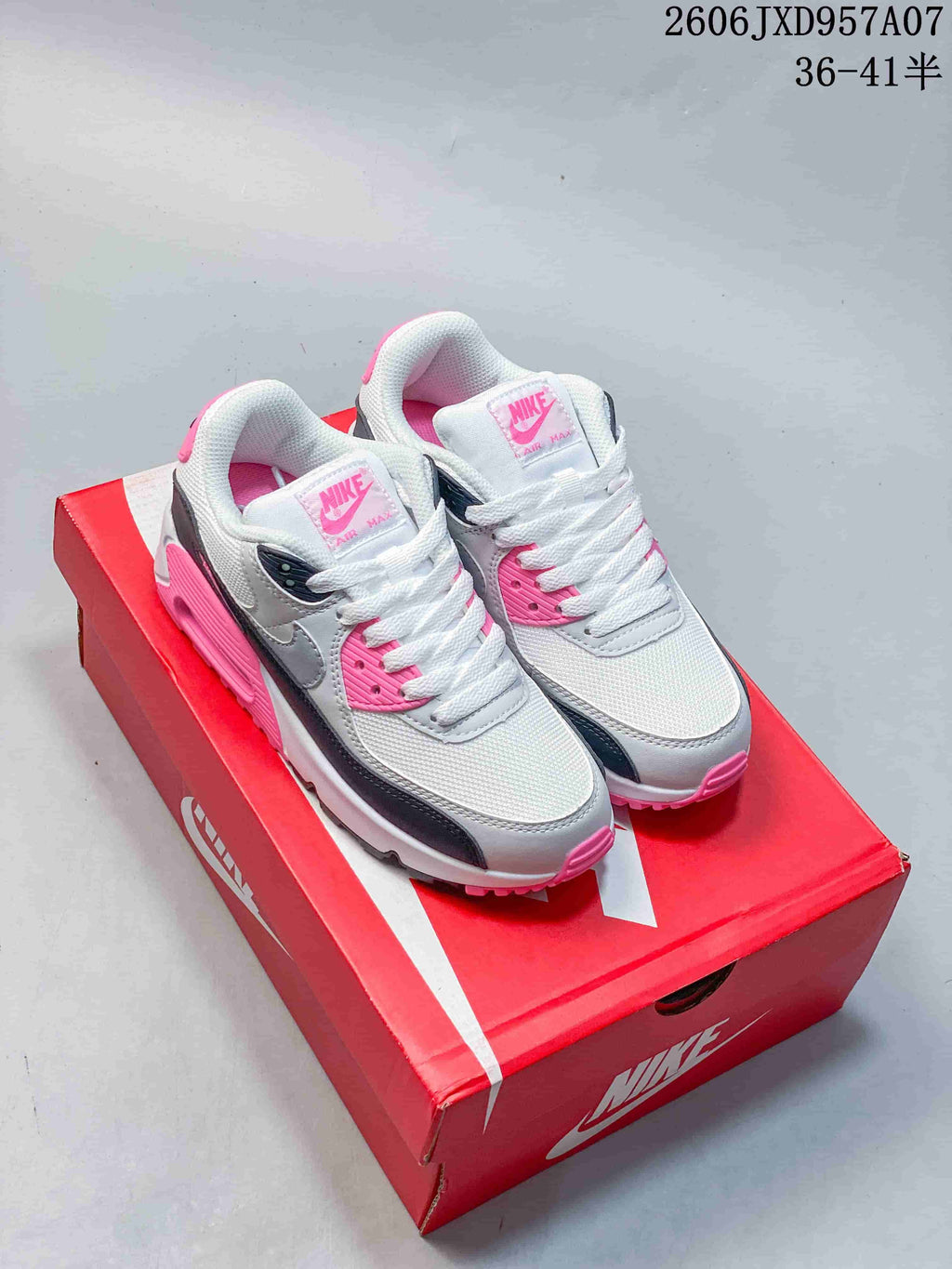 Pair of white, gray, black, and pink Nike Air Max 90 sneakers on a red shoebox