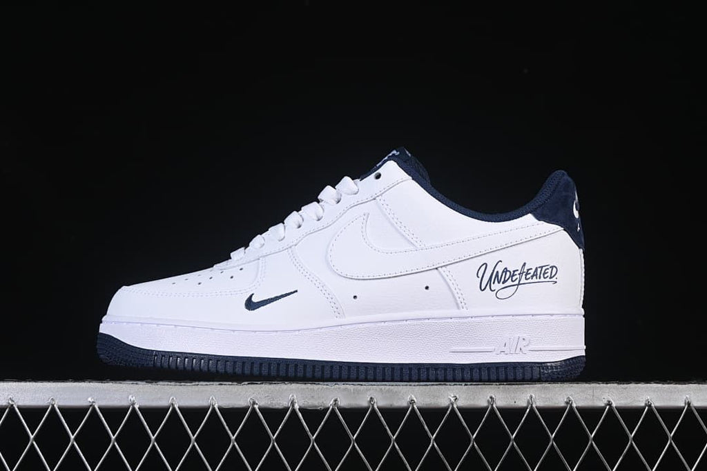 Side view of a white and navy Air Force 1-style sneaker with Undefeated lettering