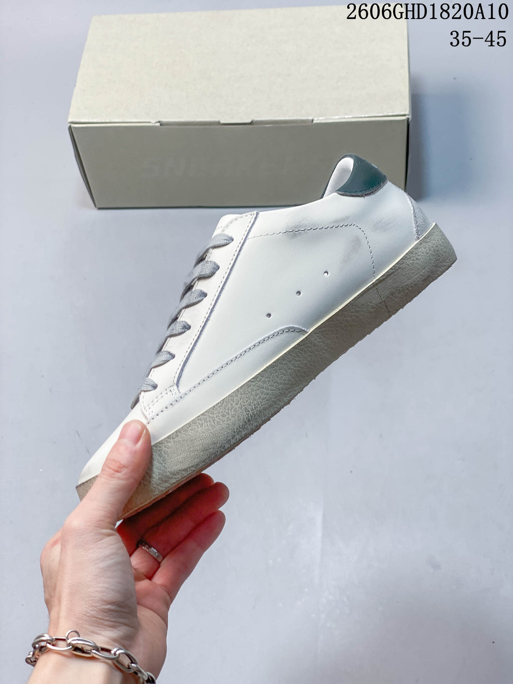 Side profile of the white sneaker with perforations, gray laces, and a dark green heel tab.