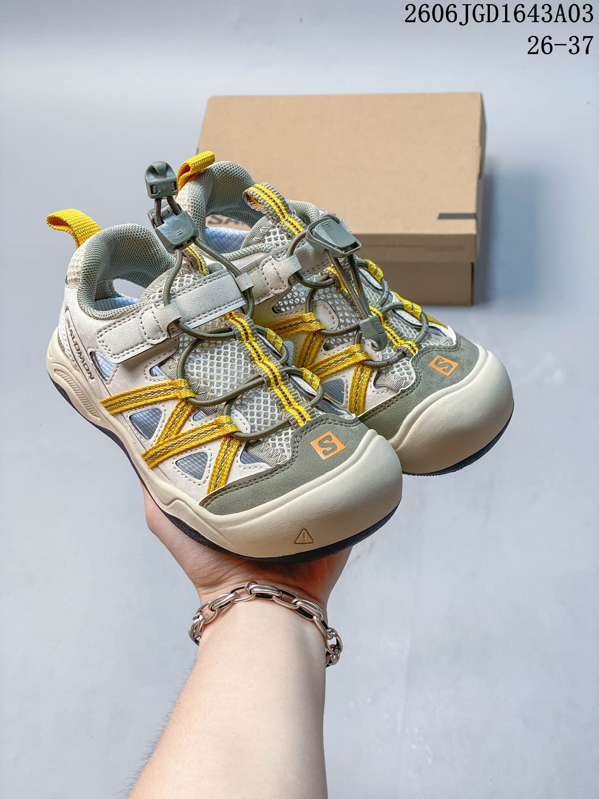 Pair of light neutral kids’ Salomon sneakers with yellow cord accents and gray details.