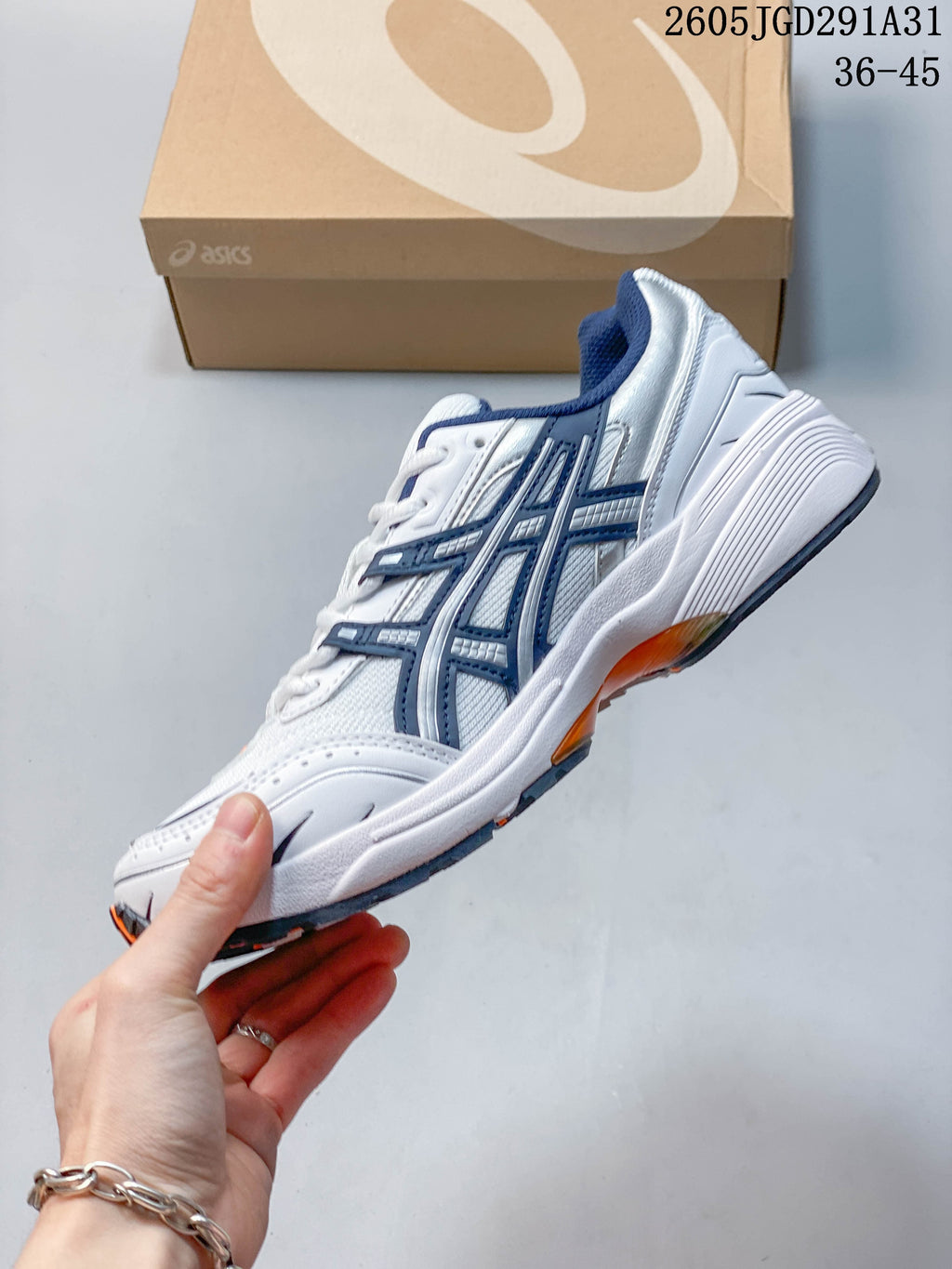 Side profile of a white sneaker with navy overlays and orange outsole accents.