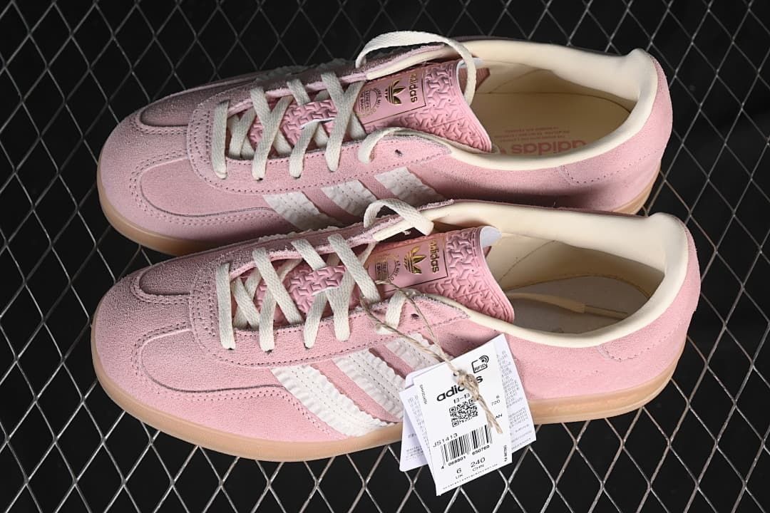 Pair of pink Gazelle Indoor sneakers with white stripes and attached product tag