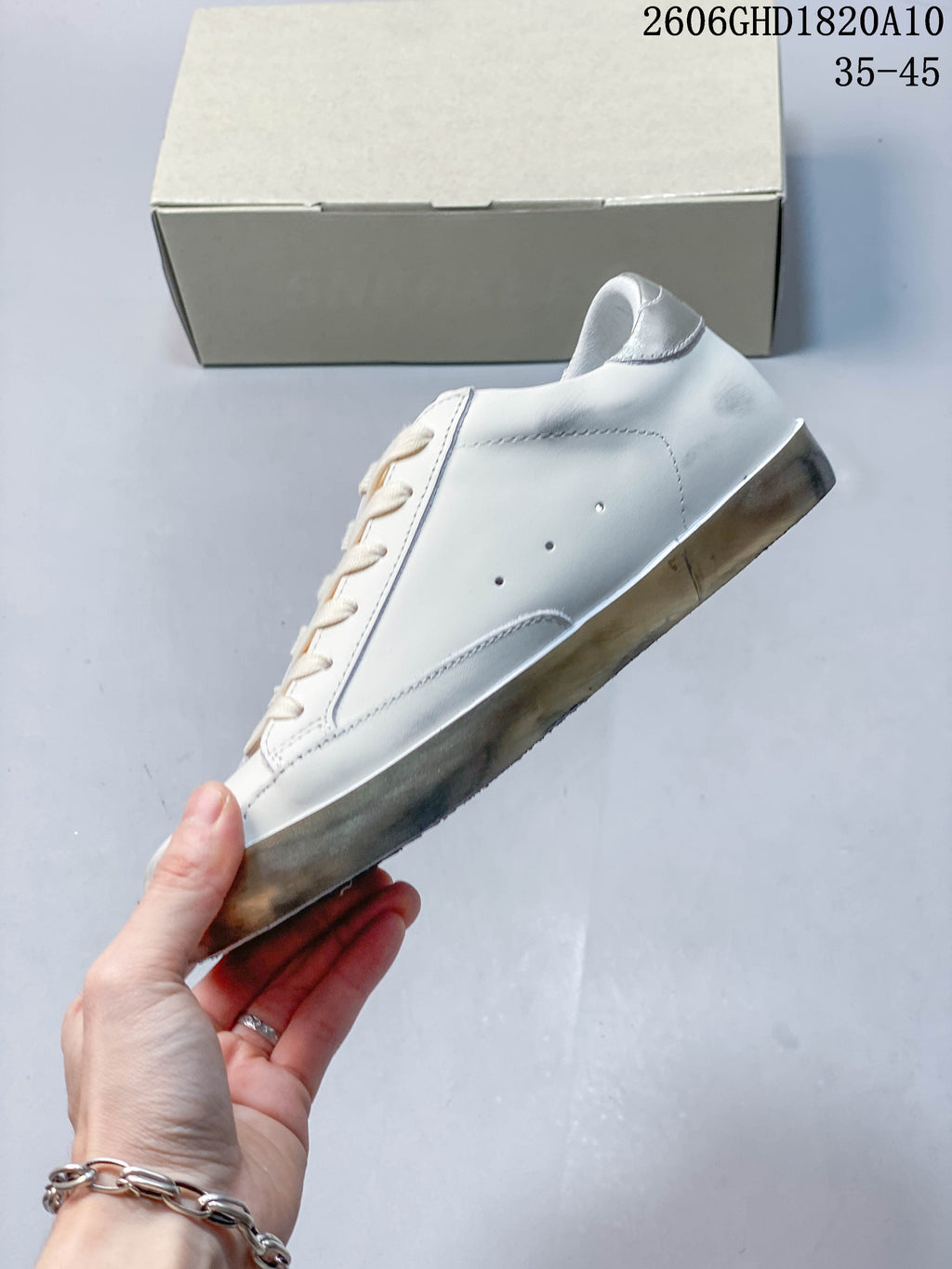 Side profile of the white sneaker showing perforations and a silver-toned heel detail.