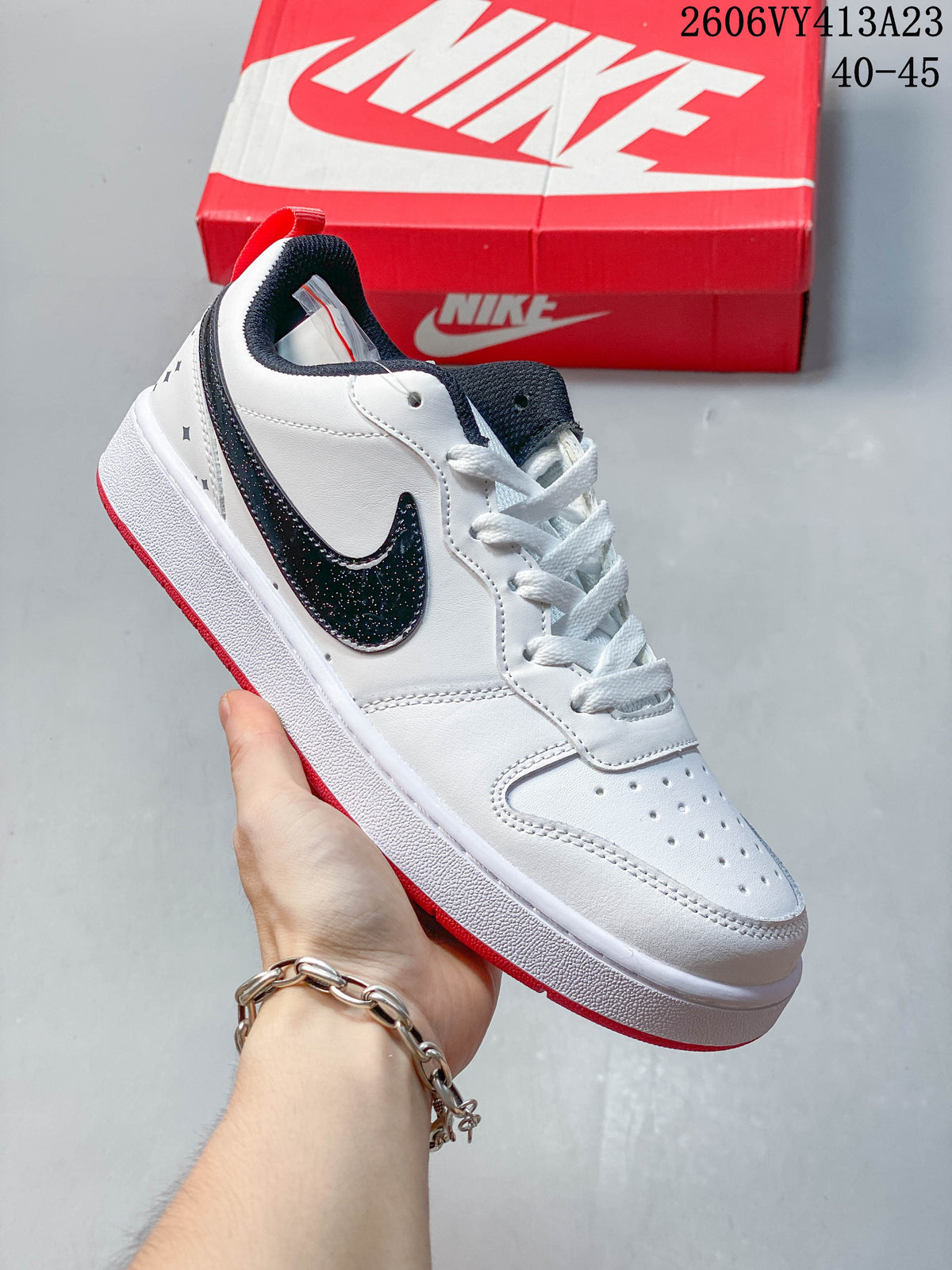 White sneaker with a black speckled Swoosh, navy collar, and red outsole accents