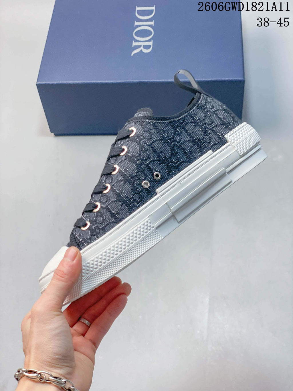 Side view of a gray patterned low-top sneaker with dark laces, white sole, and blue shoe box behind it