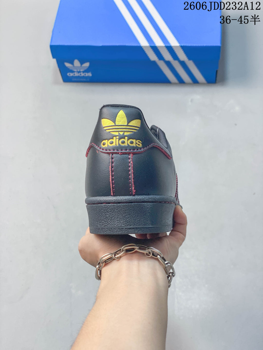 Rear view of the sneaker showing a gold-colored trefoil-style heel logo and red stitching.