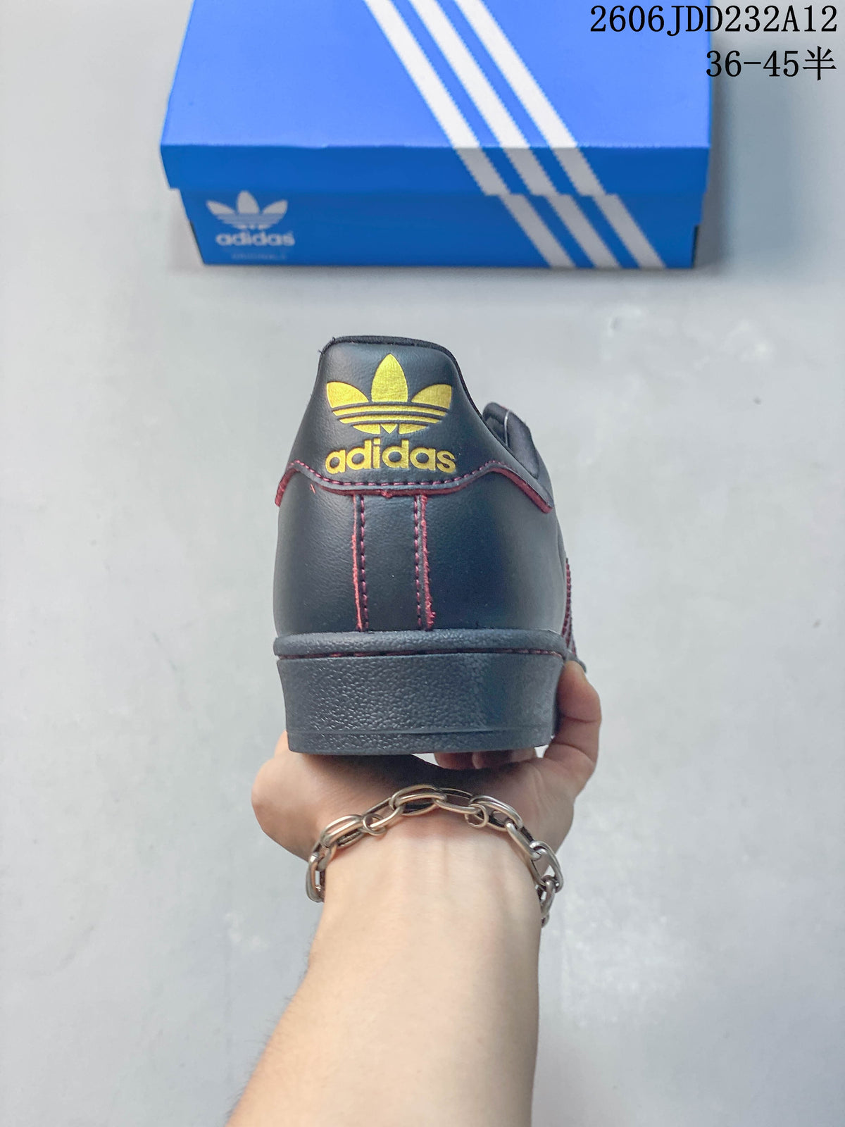 Rear view of the sneaker showing a gold-colored trefoil-style heel logo and red stitching.