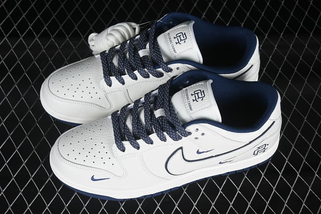 Angled top view of a pair of white and navy Nike SB Dunk Low sneakers with perforated toe panels and branded tongues.