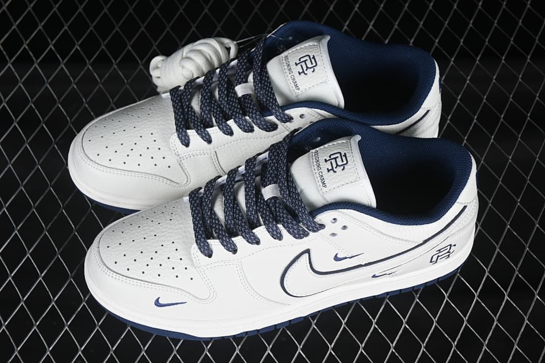 Angled top view of a pair of white and navy Nike SB Dunk Low sneakers with perforated toe panels and branded tongues.