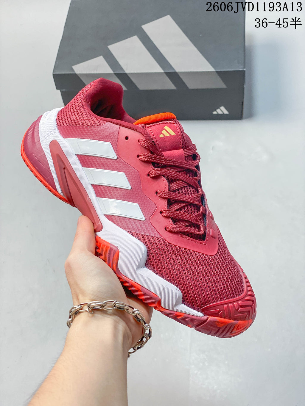 Side view of the red tennis shoe with white stripes and orange accents.
