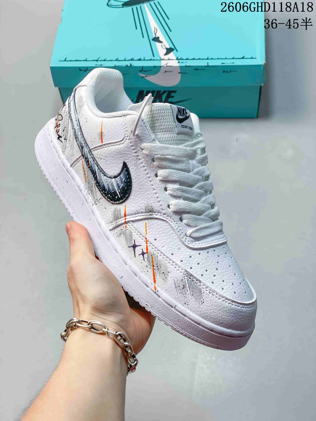 Angled view of a white low-top sneaker with dark logo and gray, black, and orange graphic accents.