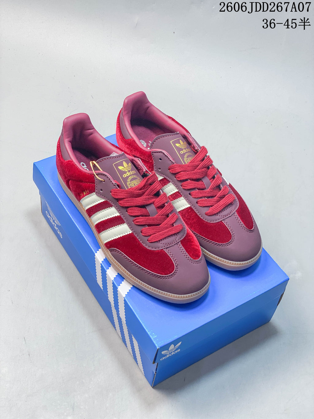 Red and mauve low-top Samba sneakers with contrasting side stripes and gum-look soles on a blue box