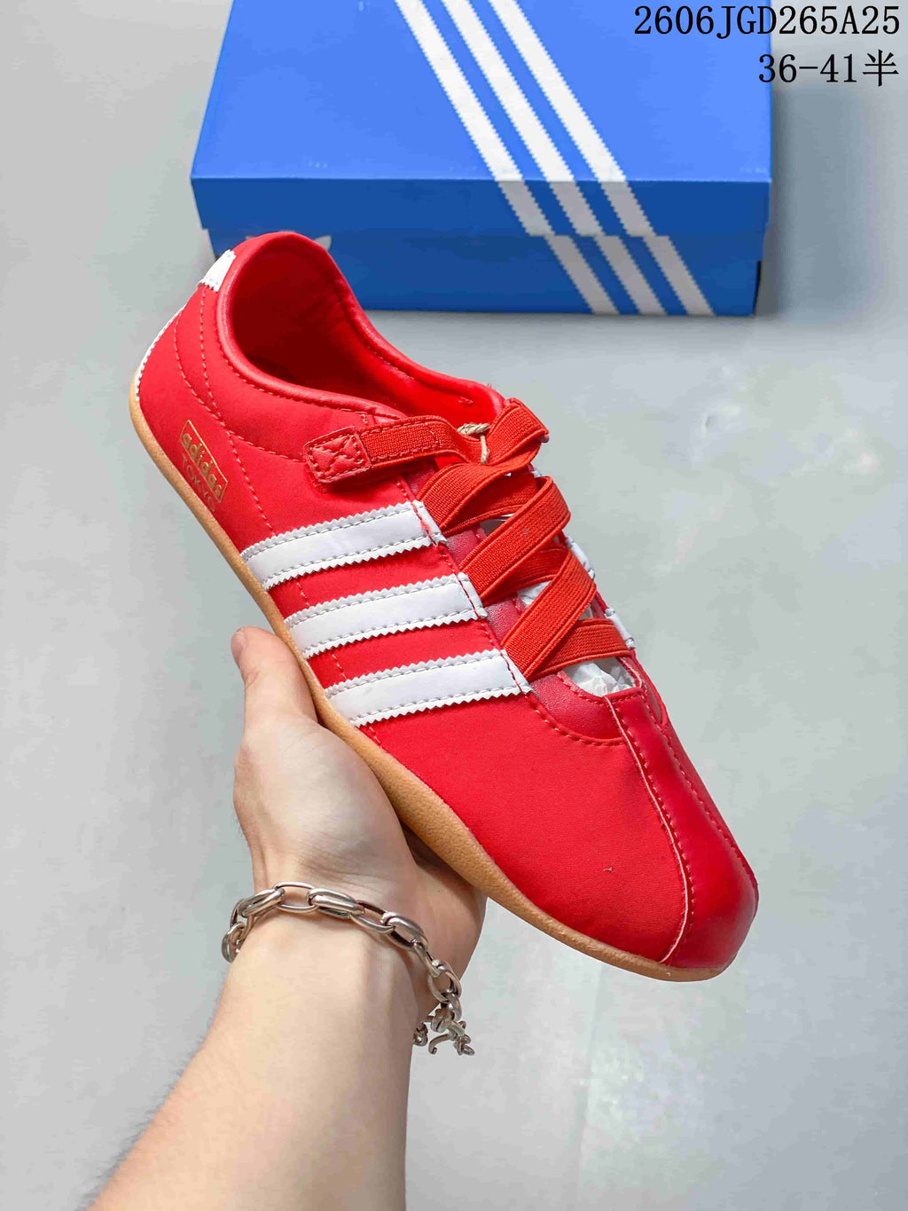 Close-up of a red Adidas Tokyo W sneaker with white side stripes, crossing bands, and a gum-colored outsole.