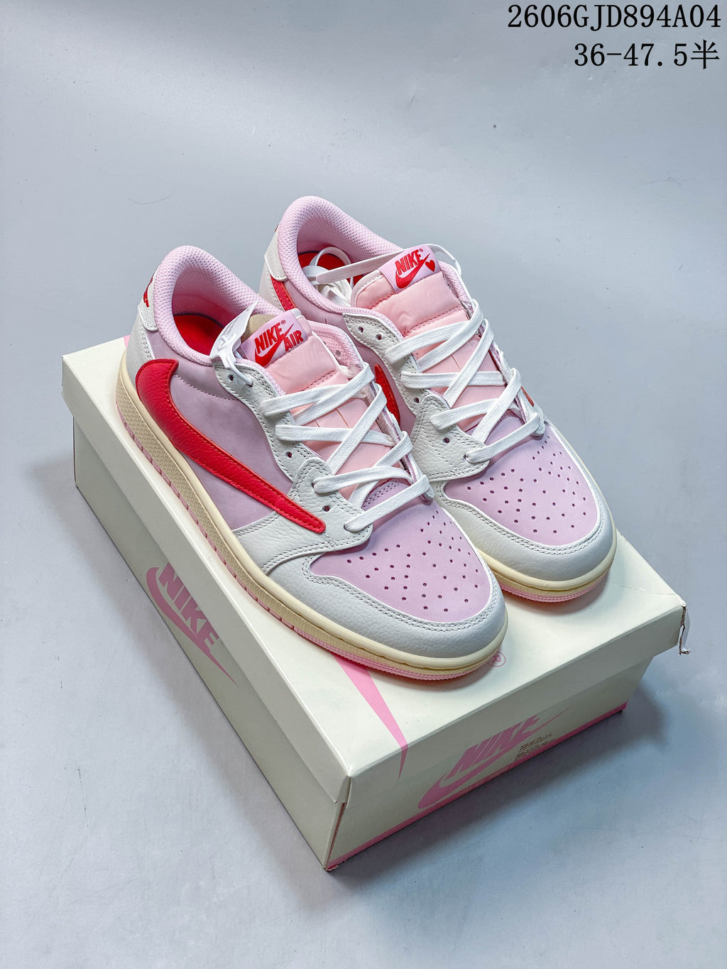 Pair of pink, white, and red low-top Air Jordan 1 OG sneakers on a shoebox