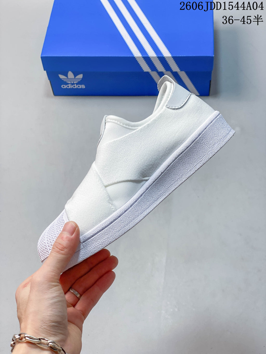 Side view of the white slip-on sneaker with crossing elastic bands and a textured shell toe.