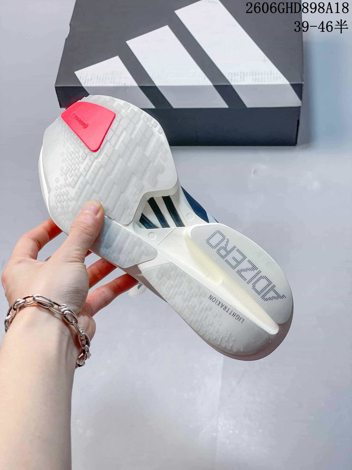 View of the outsole of a white Adizero running shoe, with the shoebox in the background.