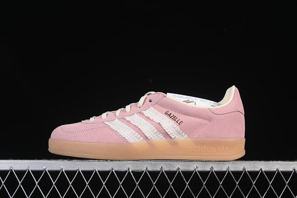 Side view of a pink adidas Gazelle Indoor sneaker with white stripes and a gum-tone sole