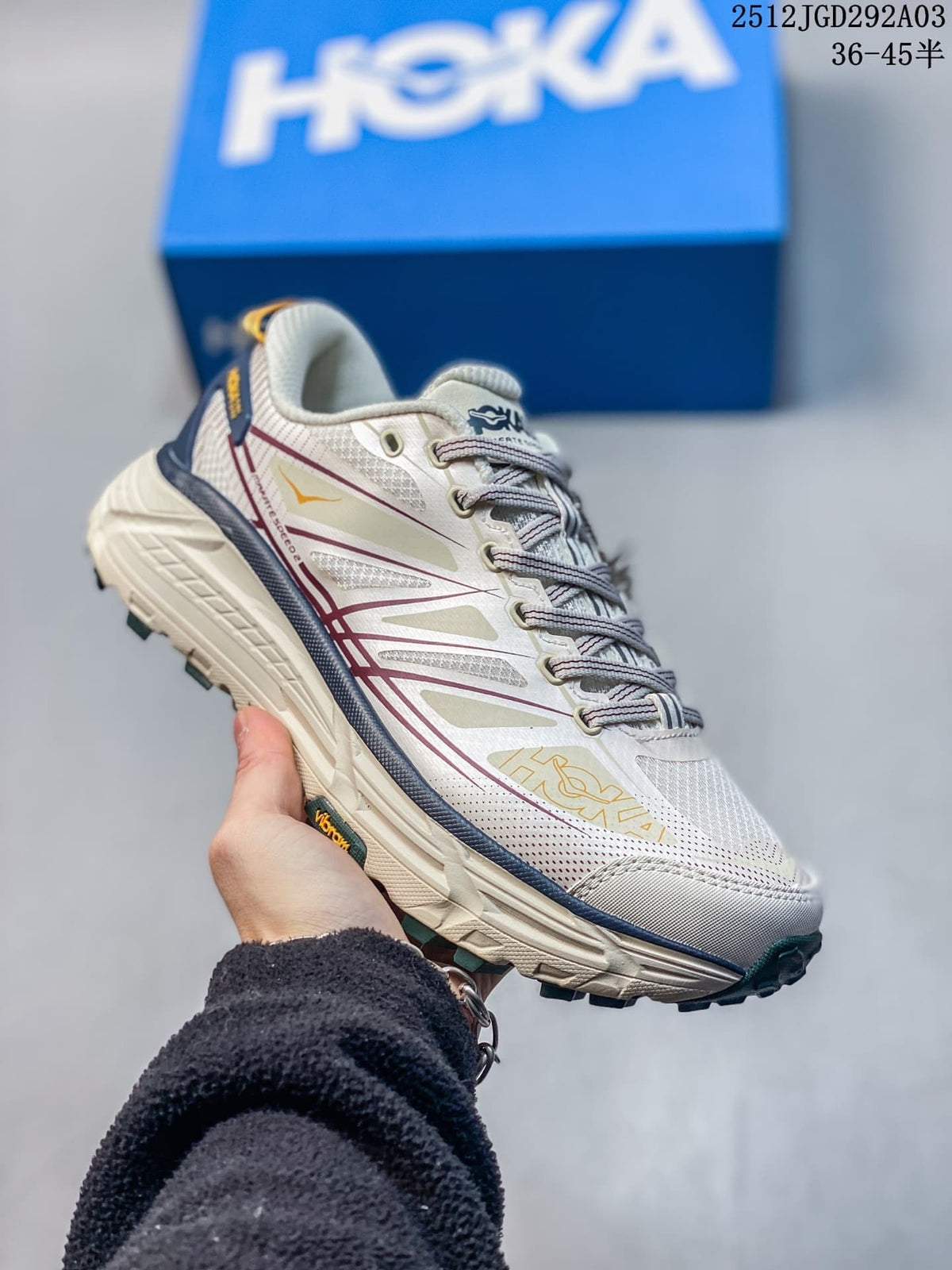 Side view of an off-white HOKA Mafate Speed 2 trail shoe with burgundy accents and a lugged outsole.