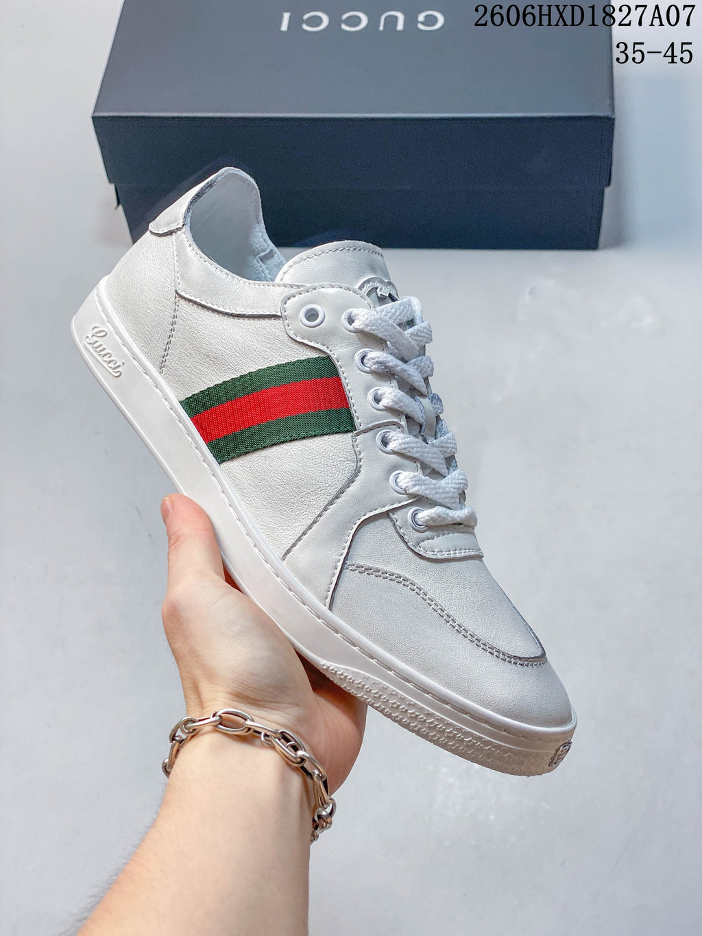 Angled side view of a white sneaker with green-and-red stripe and stitched panels.