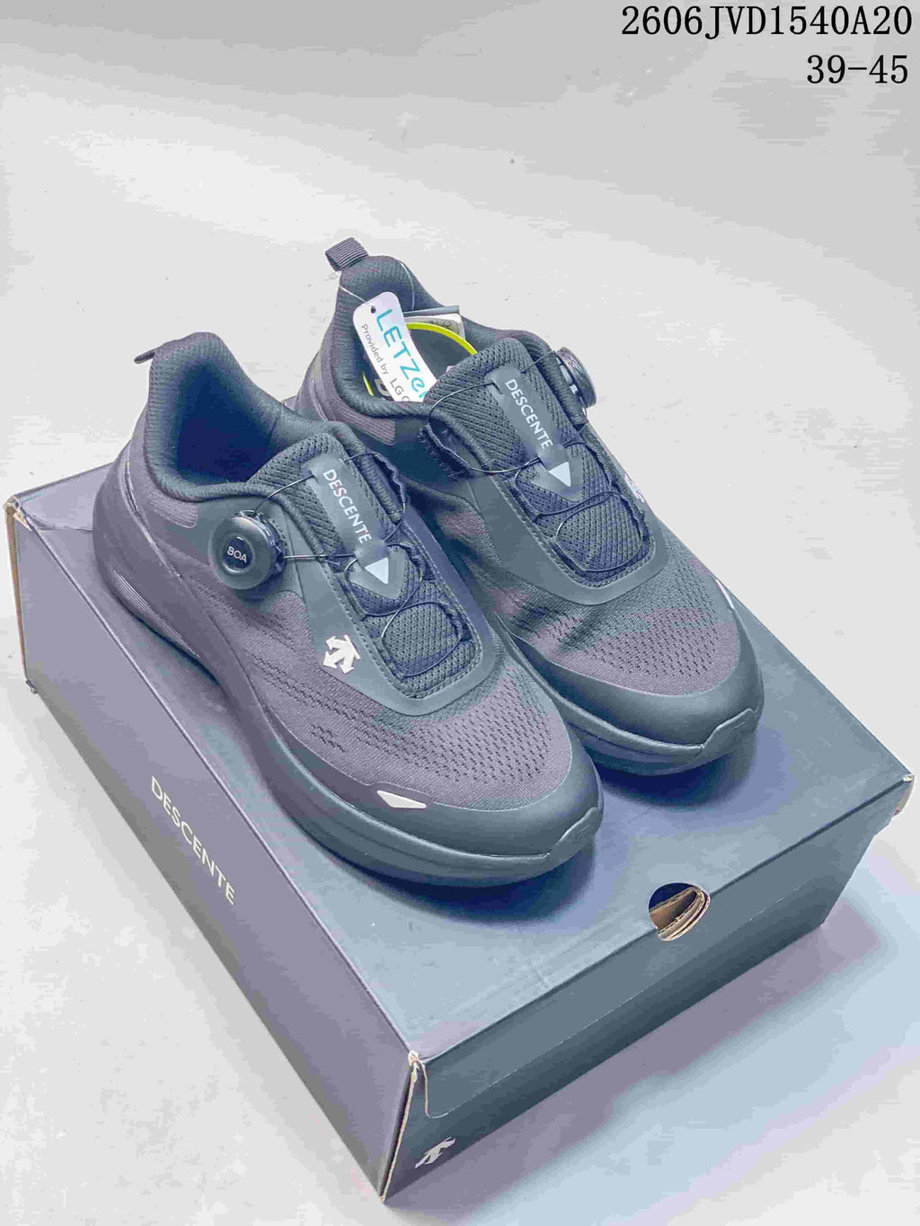 Pair of charcoal gray Descente sneakers with dial closures displayed on a box