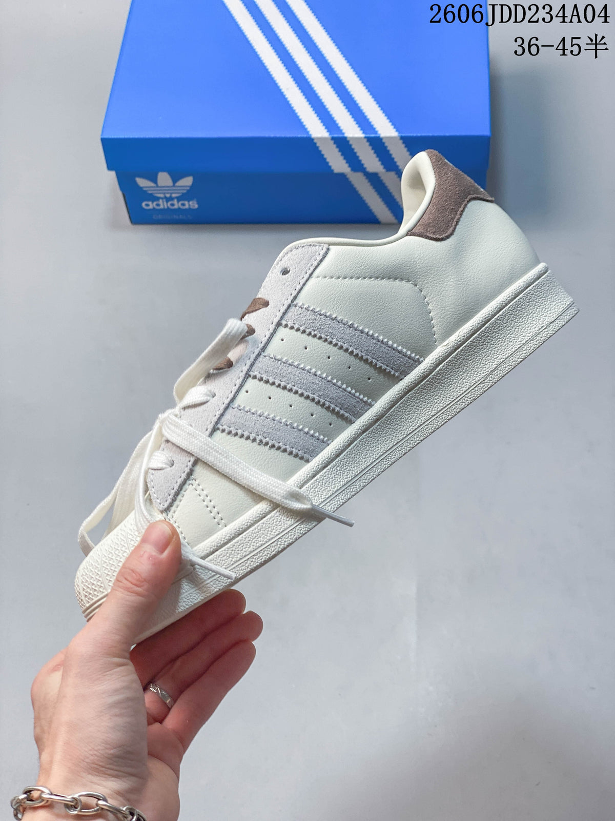 Side view of an off-white Adidas Superstar sneaker with three stripes and a textured shell toe.