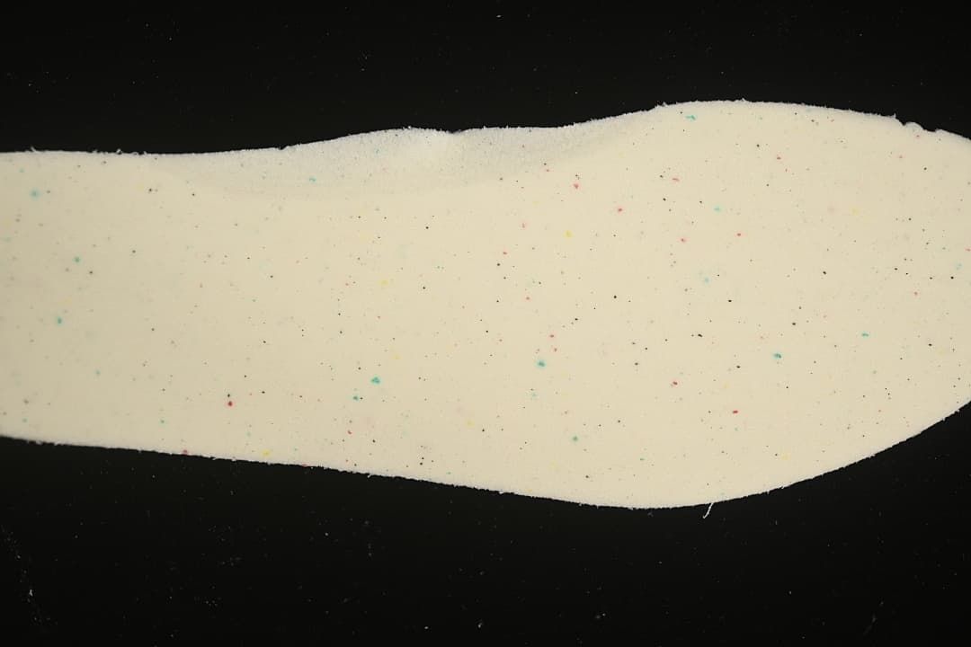 Close-up of a light-colored shoe component with small multicolor speckles.