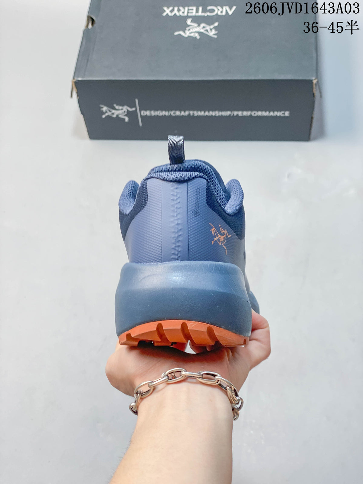 Rear view of a blue-toned outdoor shoe with orange outsole