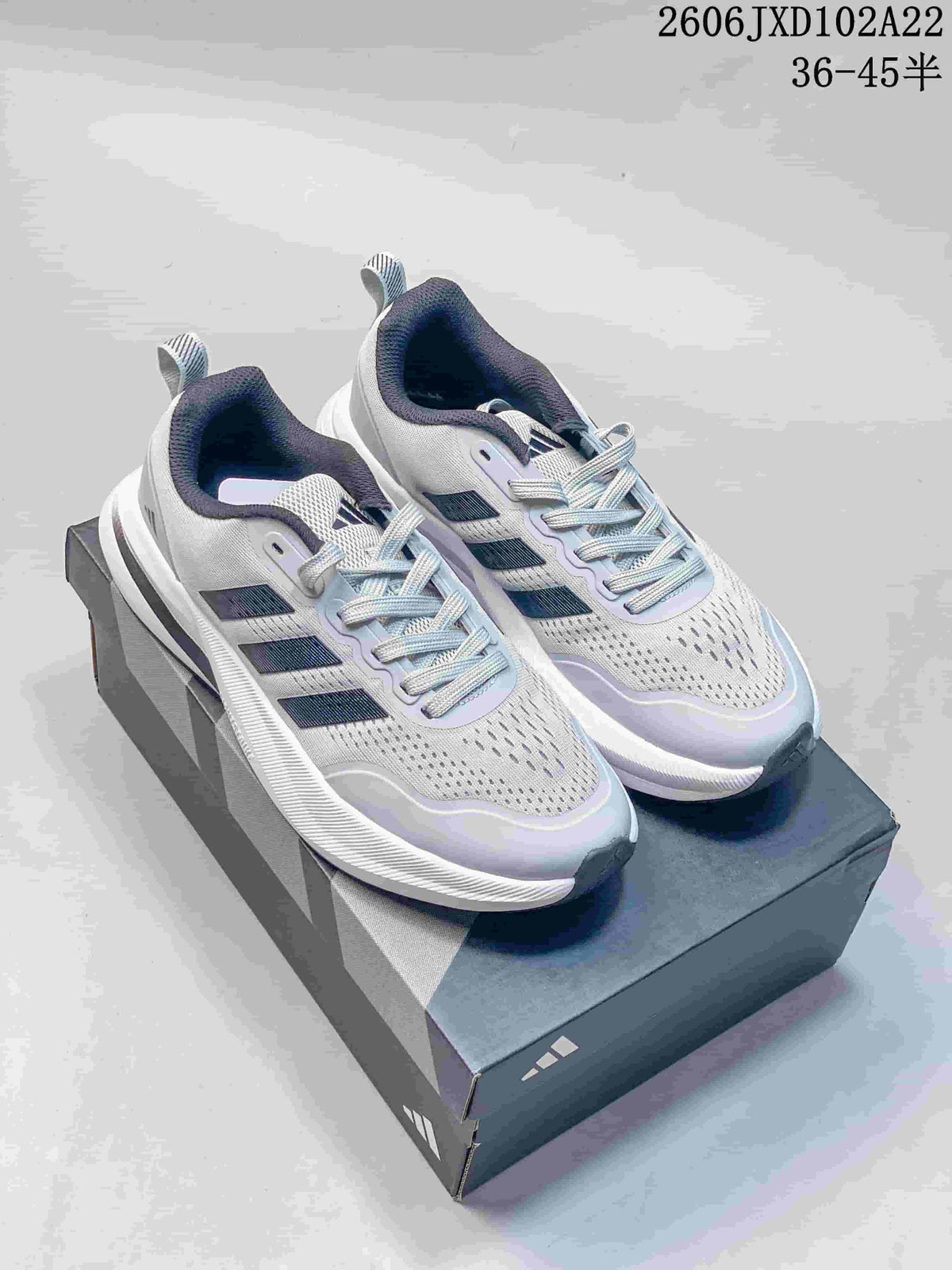 Pair of white Adidas sneakers with dark stripes, shown on a shoebox.