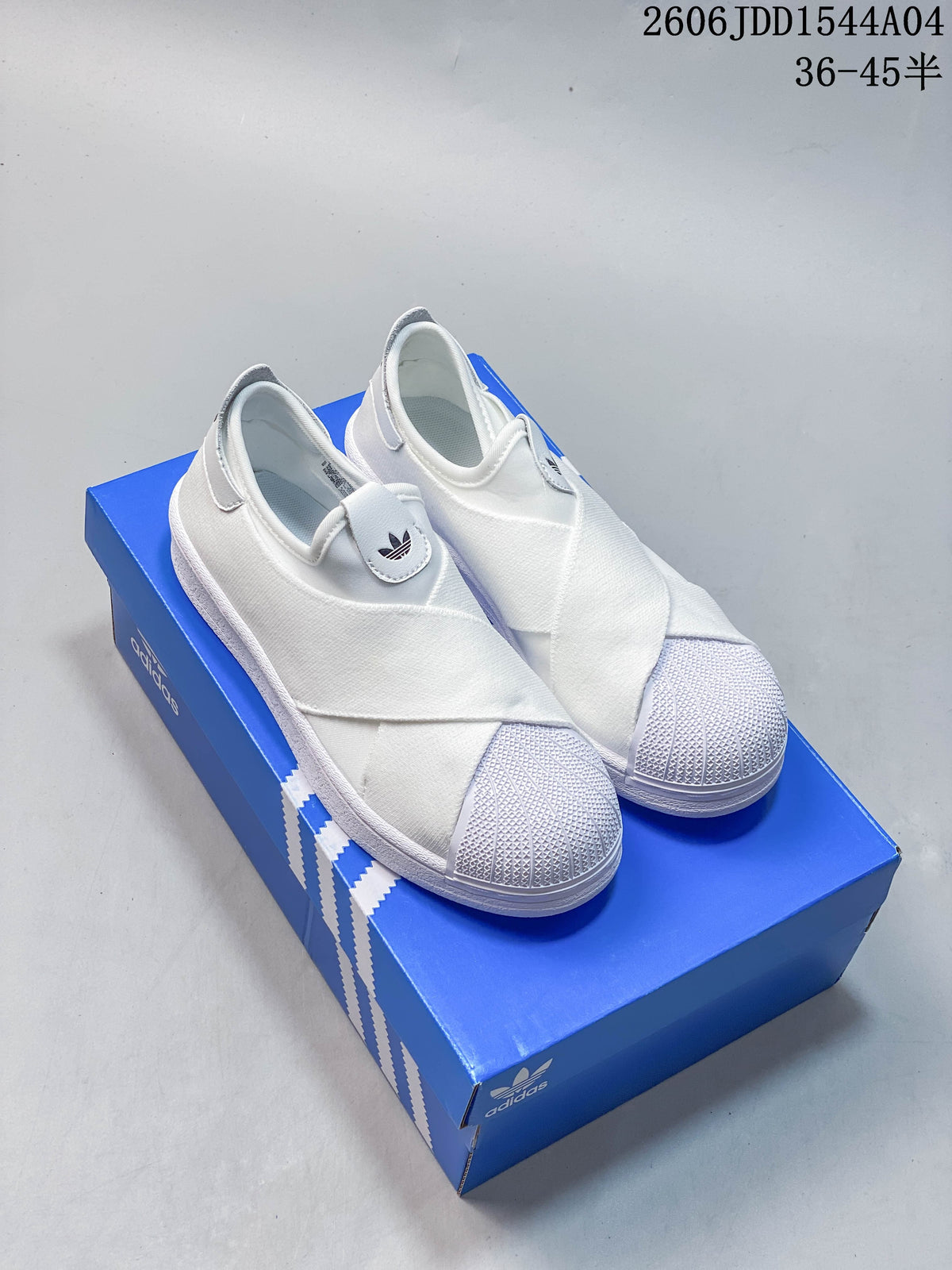 White Adidas Originals Superstar-style slip-on sneakers with textured shell toes, shown on a blue shoebox.