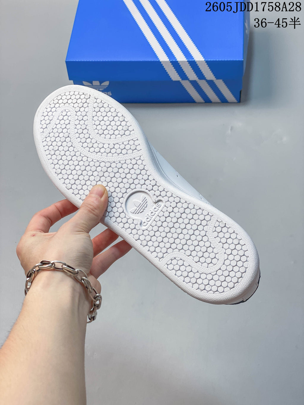 Underside of a white sneaker showing a patterned outsole, with a blue shoe box in the background.
