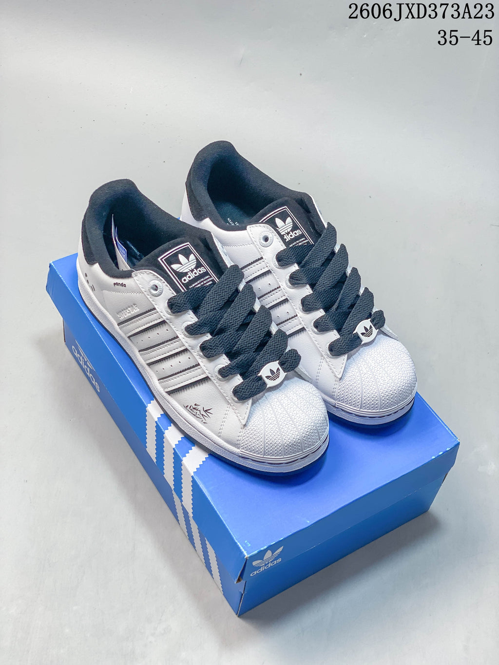 White and black Adidas Originals Superstar sneakers displayed on a blue shoebox