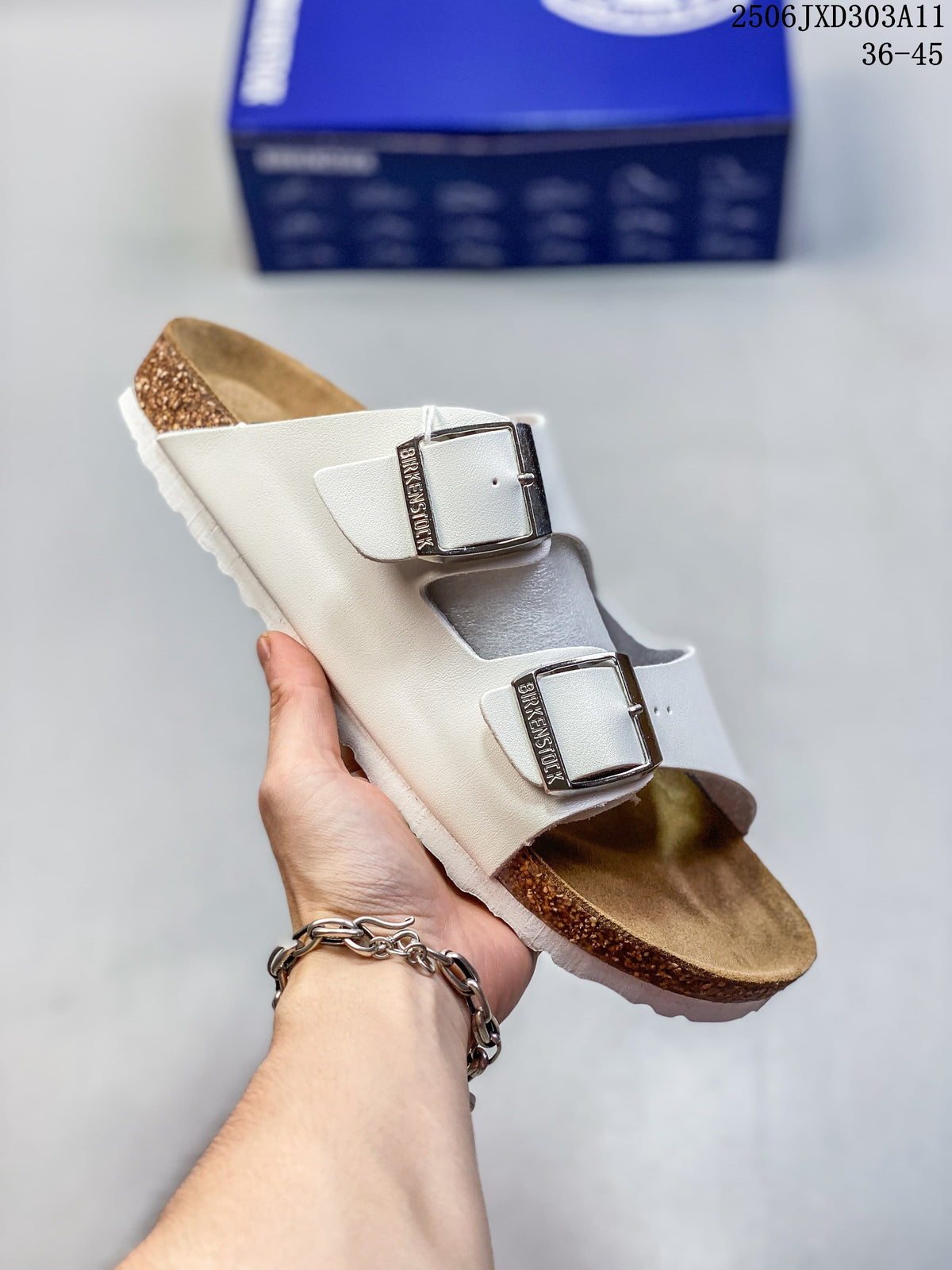 Angled view of a white two-strap sandal with silver-tone buckles and a brown footbed.