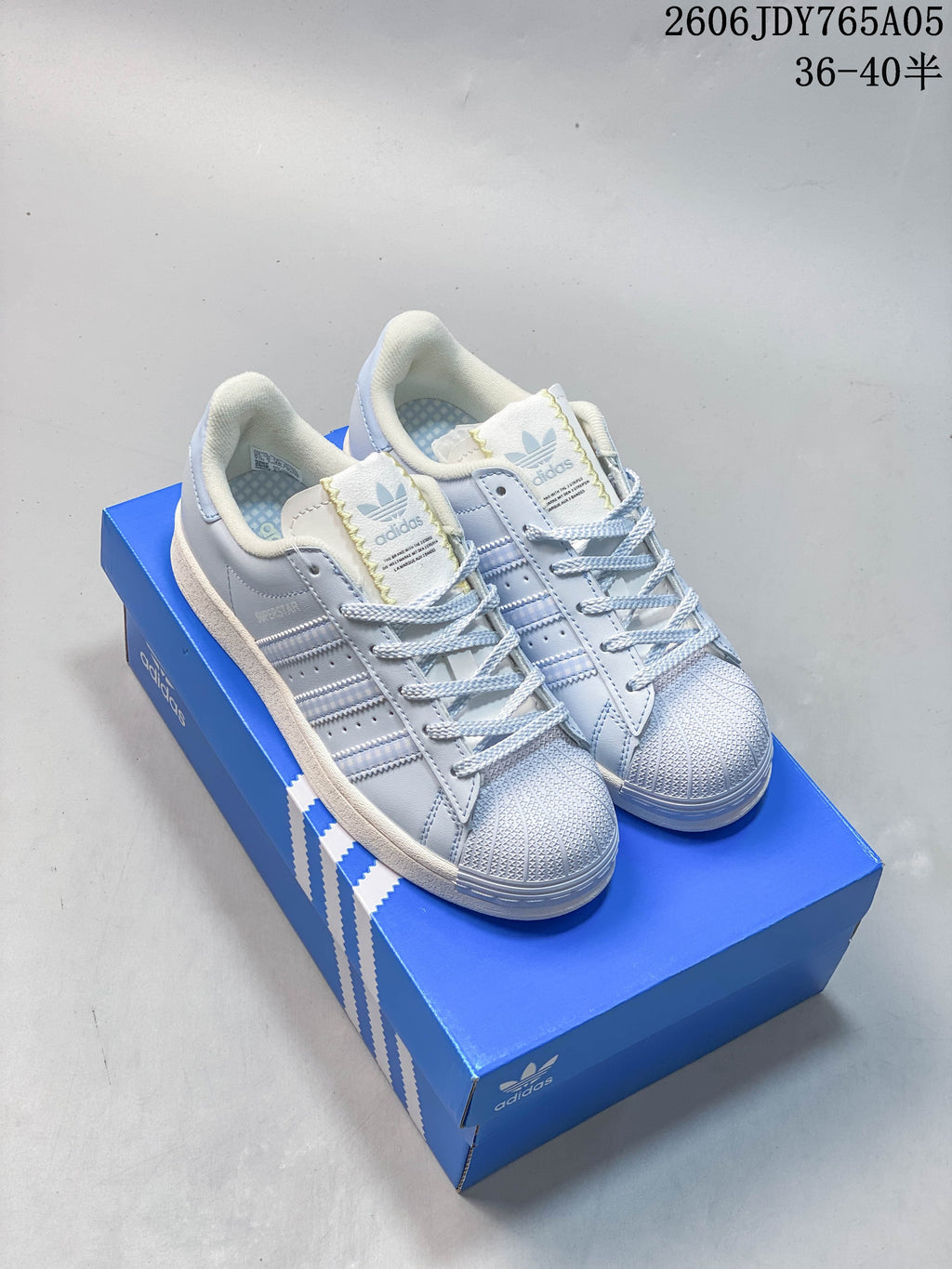 Pair of pale blue Superstar sneakers with shell toes and lace-up fastening on a blue shoebox