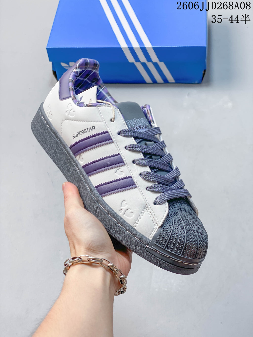 Side view of a white and purple Superstar 2 sneaker with plaid lining and a dark shell toe.