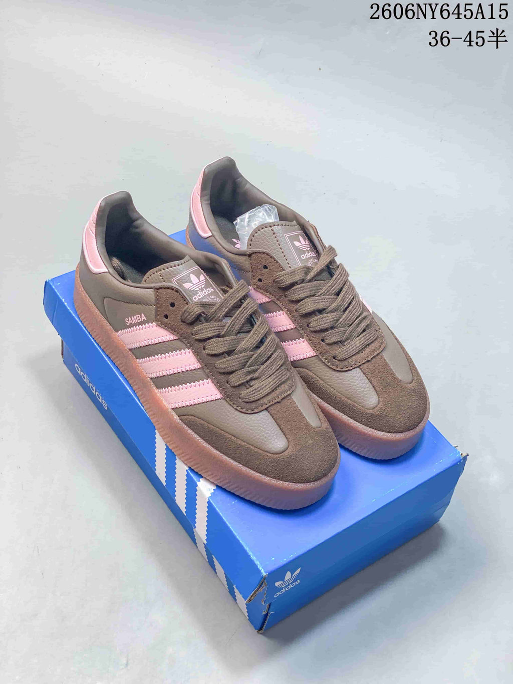 Brown Adidas Sambae sneakers with pink side stripes and a raised gum-look sole on a blue shoe box.