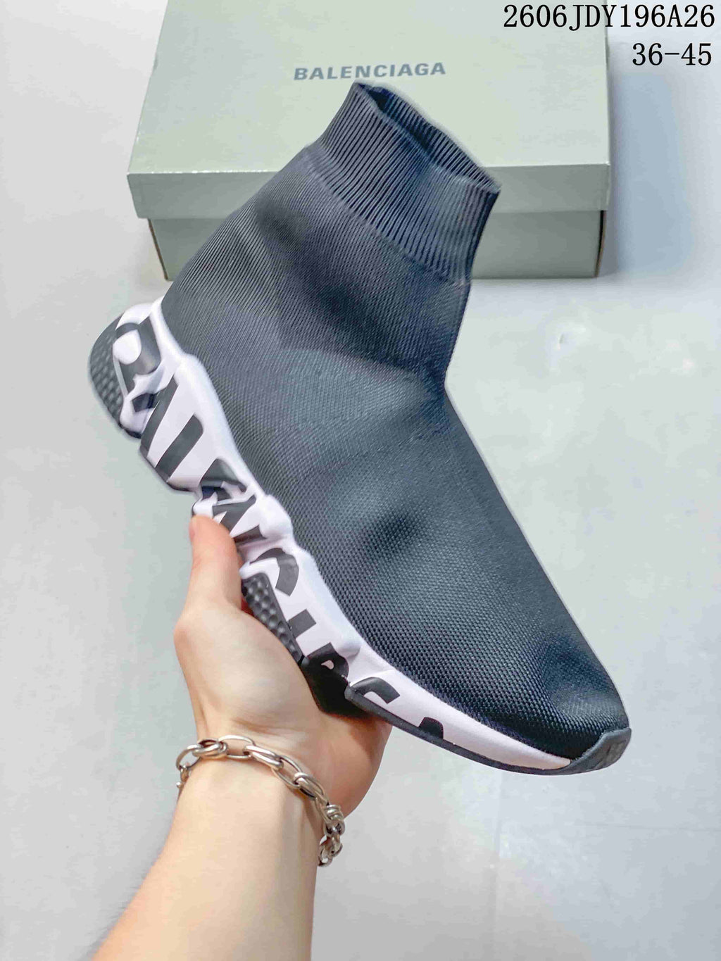 Close view of a plain dark gray sock-style sneaker with a white logo-patterned sole.