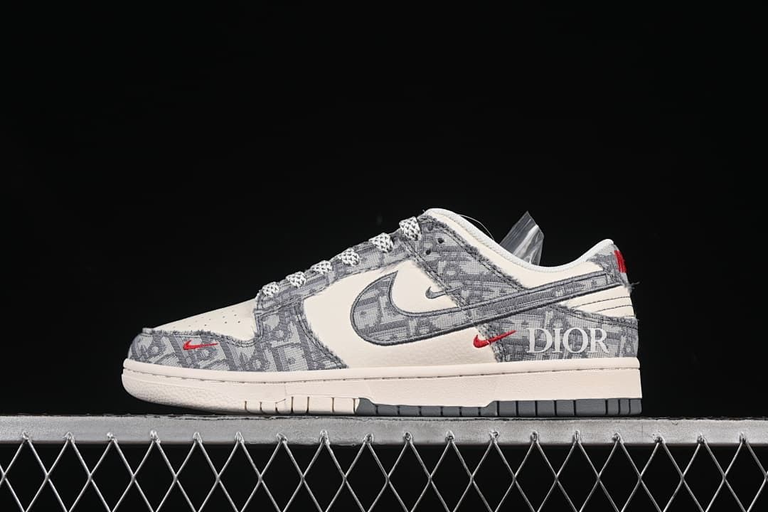 Side view of an ivory and gray low-top Nike SB Dunk with monogram-style panels and red accents