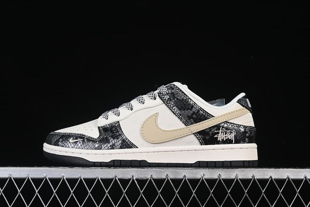 Side view of an off-white and black Nike SB Dunk Low sneaker with snakeskin-pattern panels and a light tan Swoosh.