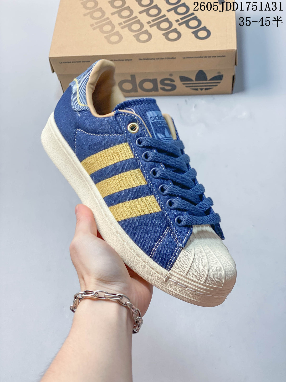 Angled view of a blue denim-look Adidas Superstar sneaker with gold-tone stripes and a cream shell toe