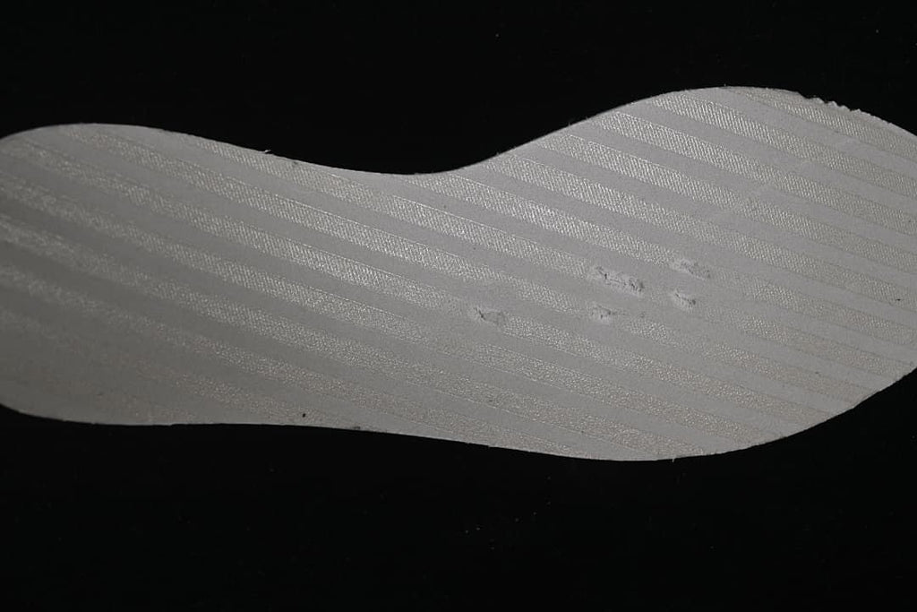 Close-up of a pale shoe component against a dark background.